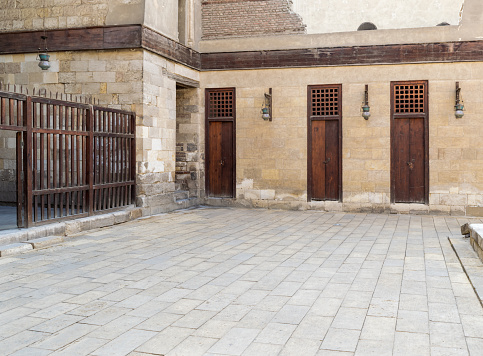 Three adjacent doors in a stone bricks wall and wooden fence at the main courtyard of public historic mosque of Sultan Al Nassir Qalawun, Cairo, Egypt