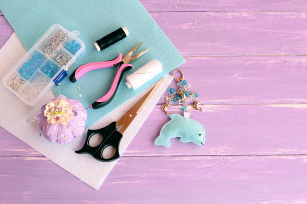 Funny felt dolphin keychain. Home felt plush keychain, bag decor. Handmade car keyring. A set of tools and materials for children's craft and sewing. Lilac wooden background with empty place for text