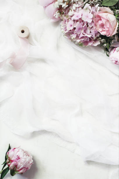 istock Feminine floral frame composition. Beautiful pink peonies, hydrangea and roses flowers on white muslin table runner background. Empty space. Wedding styled stock photo. Vertical flat lay, top view. 1175184240
