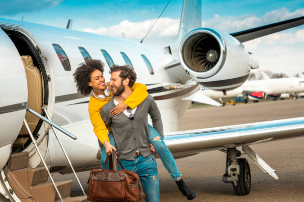 hombre rico dando con entusiasmo a su pareja un paseo a la cabeza junto a un jet privado en un aeropuerto asfalto - status symbol audio fotografías e imágenes de stock