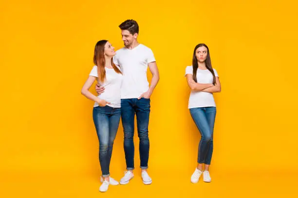 Full size phot of sullen girl looking at sweethearts cuddling wearing, white t-shirts denim jeans isolated over yellow background