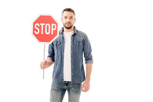 front view of bearded man man in denim shirt holding stop sign isolated on white