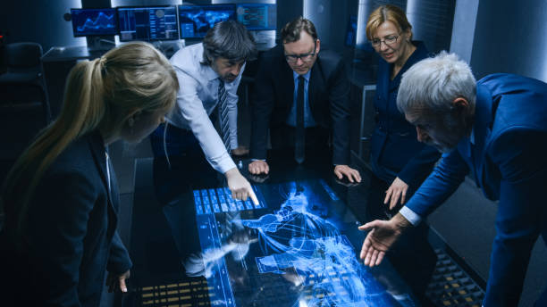 istock Team of Government Intelligence / FBI Agents Standing Around Digital Touch Screen Table and Tracking Suspect Vehicle Using Satellite Surveillance in the Monitoring Room. 1175197099