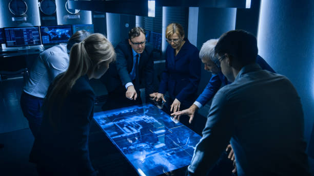 istock Team of Government Intelligence / FBI Agents Standing Around Digital Touch Screen Table and Tracking Suspect Vehicle Using Satellite Surveillance in the Monitoring Room. 1175197129