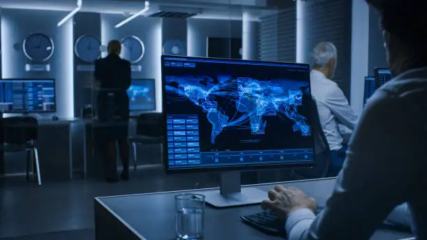 Back View of the Cyber Security Officer Working on Personal Computer Showing Traffic Data Flow in the System Control Room full of Special Intelligence Agents.