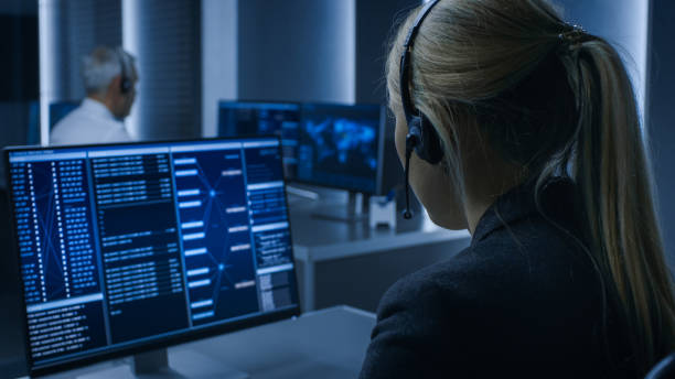 vue arrière de la femme contrôleur portant casque travaillant sur l'ordinateur personnel, processus de surveillance dans la salle de contrôle du système pleine d'agents de renseignement spéciaux. - dispatcheur photos et images de collection