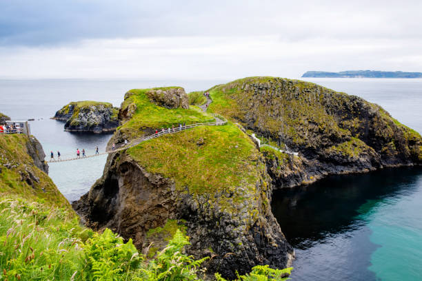 carrick-a-rede rope bridge, famoso puente de cuerda cerca de ballintoy en el condado de antrim, irlanda del norte. atracción turística, puente a la pequeña isla en día nublado. - carrick a rede fotografías e imágenes de stock