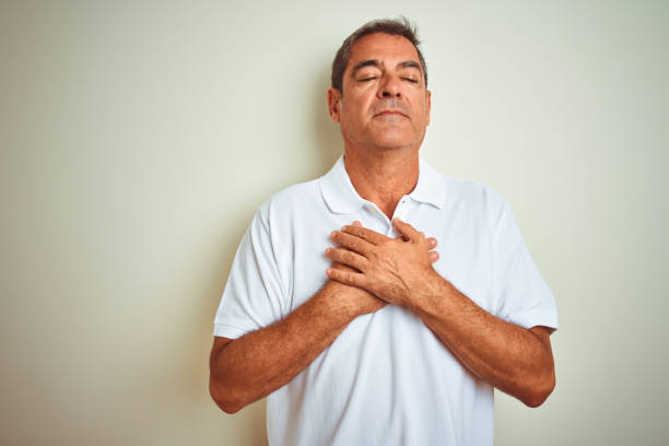 istock Handsome middle age man wearing polo standing over isolated white background smiling with hands on chest with closed eyes and grateful gesture on face. Health concept. 1175200380