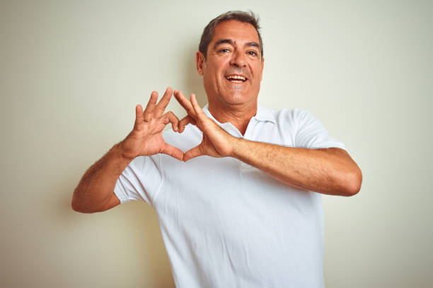 Handsome middle age man wearing polo standing over isolated white background smiling in love showing heart symbol and shape with hands. Romantic concept.