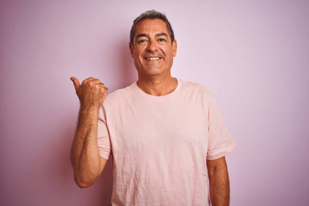 istock Handsome middle age man wearing t-shirt standing over isolated pink background smiling with happy face looking and pointing to the side with thumb up. 1175201418