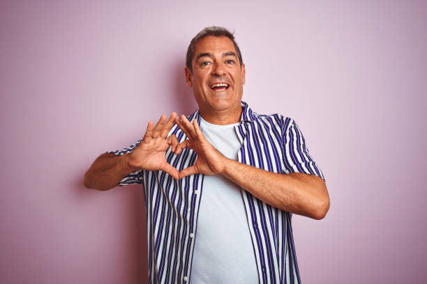 istock Handsome middle age man wearing striped shirt standing over isolated pink background smiling in love showing heart symbol and shape with hands. Romantic concept. 1175201577
