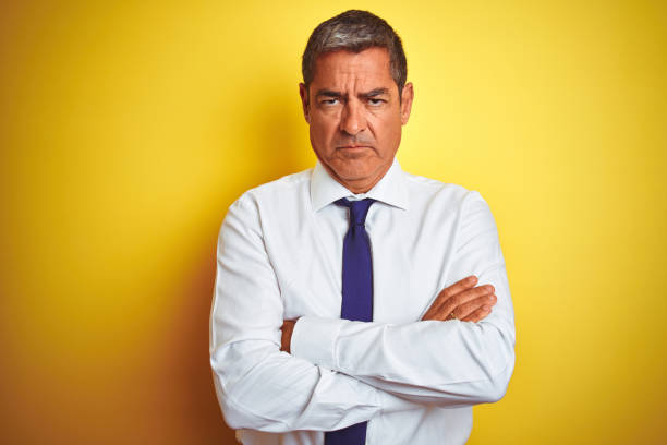 homem de negócios considerável da idade média que está sobre o fundo amarelo isolado céptico e nervoso, desaprovando a expressão na face com braços cruzados. pessoa negativa. - businessman business arms crossed business person - fotografias e filmes do acervo