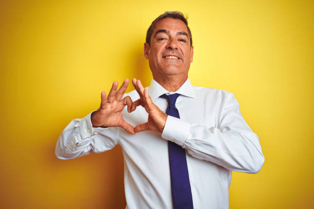 istock Handsome middle age businessman standing over isolated yellow background smiling in love doing heart symbol shape with hands. Romantic concept. 1175202096