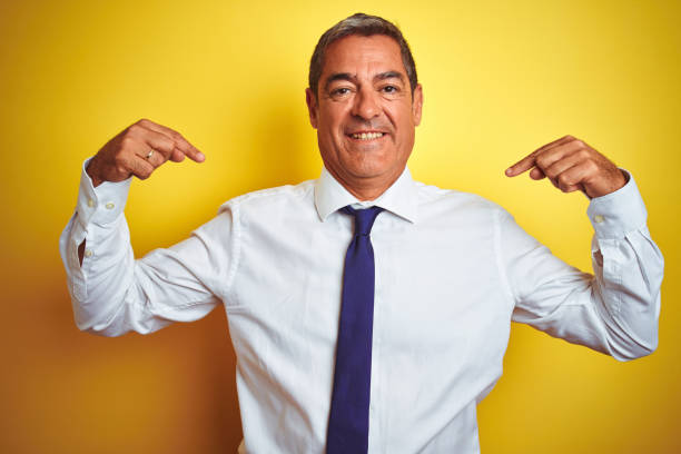 istock Handsome middle age businessman standing over isolated yellow background looking confident with smile on face, pointing oneself with fingers proud and happy. 1175202119