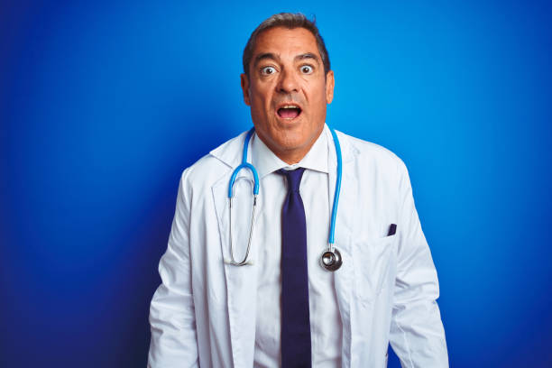 istock Handsome middle age doctor man wearing stethoscope over isolated blue background afraid and shocked with surprise expression, fear and excited face. 1175202331