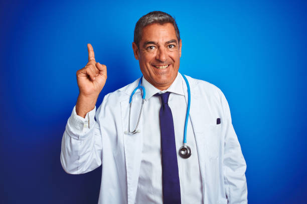 istock Handsome middle age doctor man wearing stethoscope over isolated blue background pointing finger up with successful idea. Exited and happy. Number one. 1175203003