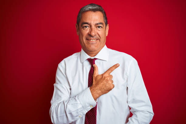 istock Handsome middle age businessman standing over isolated red background cheerful with a smile of face pointing with hand and finger up to the side with happy and natural expression on face 1175203233