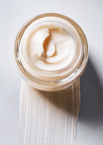 Open jar of face cream, brush stroke of cream on marble surface. Top view.