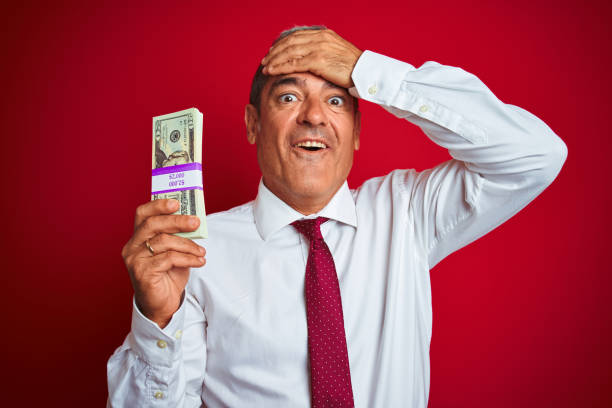 istock Handsome middle age businessman holding dollars over isolated red background stressed with hand on head, shocked with shame and surprise face, angry and frustrated. Fear and upset for mistake. 1175203450