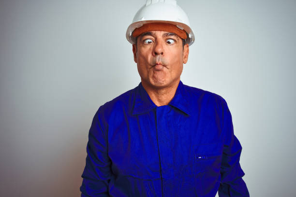 istock Handsome middle age worker man wearing uniform and helmet over isolated white background making fish face with lips, crazy and comical gesture. Funny expression. 1175204910