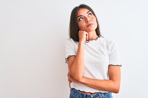 Young beautiful woman wearing casual t-shirt standing over isolated white background with hand on chin thinking about question, pensive expression. Smiling with thoughtful face. Doubt concept.