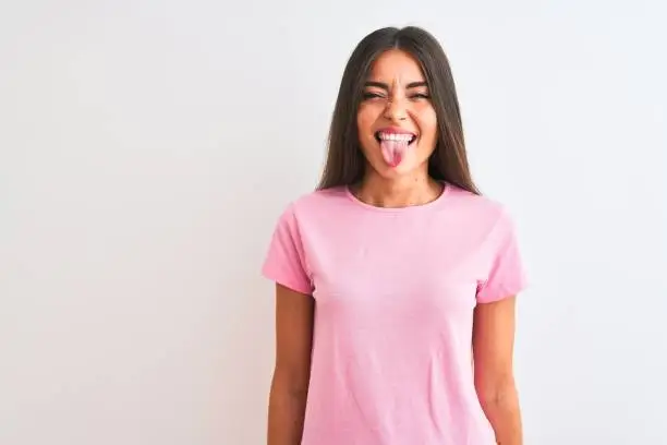 Young beautiful woman wearing pink casual t-shirt standing over isolated white background sticking tongue out happy with funny expression. Emotion concept.