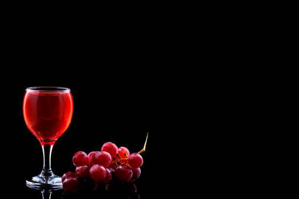 Red wine in a glass and a bottle standing on a barrel with a bunch of grapes