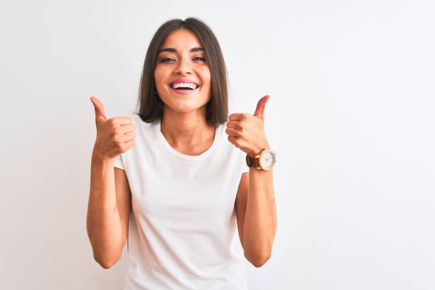 junge schöne frau trägt lässige t-shirt stehen über isolierten weißen hintergrund erfolgsschild tun positive geste mit der hand, daumen hoch lächelnd und glücklich. fröhlicher ausdruck und siegergeste. - thumbs up human thumb human finger brown hair stock-fotos und bilder