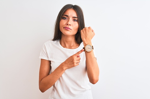 Young beautiful woman wearing casual t-shirt standing over isolated white background In hurry pointing to watch time, impatience, looking at the camera with relaxed expression