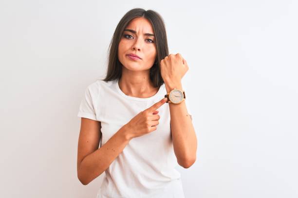 Young beautiful woman wearing casual t-shirt standing over isolated white background In hurry pointing to watch time, impatience, looking at the camera with relaxed expression Young beautiful woman wearing casual t-shirt standing over isolated white background In hurry pointing to watch time, impatience, looking at the camera with relaxed expression checking the time stock pictures, royalty-free photos & images