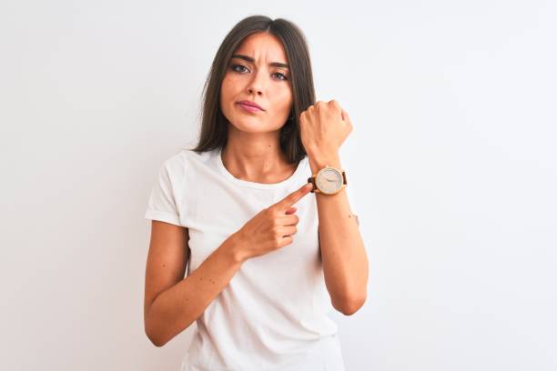 young beautiful woman wearing casual t-shirt standing over isolated white background in hurry pointing to watch time, impatience, looking at the camera with relaxed expression - clock face clock deadline human hand imagens e fotografias de stock