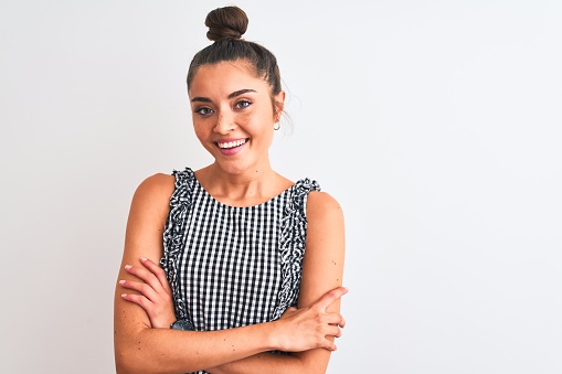 Beautiful woman with bun wearing casual dresss standing over isolated white background happy face smiling with crossed arms looking at the camera. Positive person.