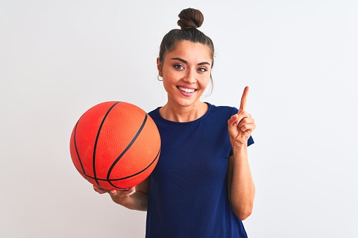 Young beautiful sportswoman holding basketball ball over isolated white background very happy pointing with hand and finger to the side