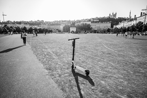 Overview of the Place Bellecour, It is one of the largest open squares in Europe. In the middle is an equestrian statue of King Louis XIV by François-Frédéric Lemot. Tourists are walking across the square with a motorised push scooter in the foreground. A typical summer day in Lyon, France