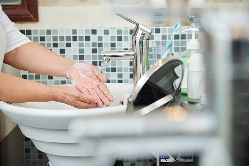 Close-up of senior woman washing her hands under the running water in the bathroom at home