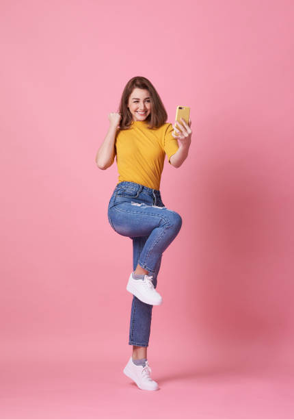 Portrait of a happy young woman celebrating with mobile phone isolated over pink background. stock photo