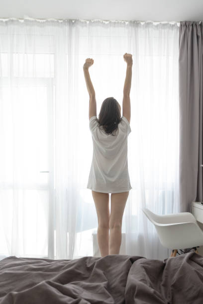 istock Woman waking up and standing near window 1175221700