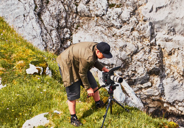 Photographer me professional video camera on a tripod next to a limestone rock at work Garmisch-Partenkirchen, August 8., 2019: Photographer me professional video camera on a tripod next to a limestone rock at work RED Camera stock pictures, royalty-free photos & images