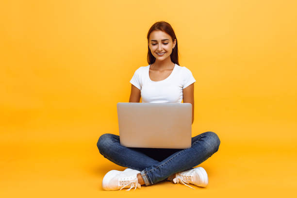 istock young woman sitting cross-legged using laptop isolated on yellow background 1175223592