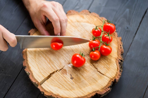istock Chef slicing cherry tomatoes on a wooden board, close-up. 1175224428