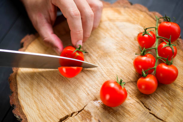 istock Chef slicing cherry tomatoes on a wooden board, close-up. 1175224485