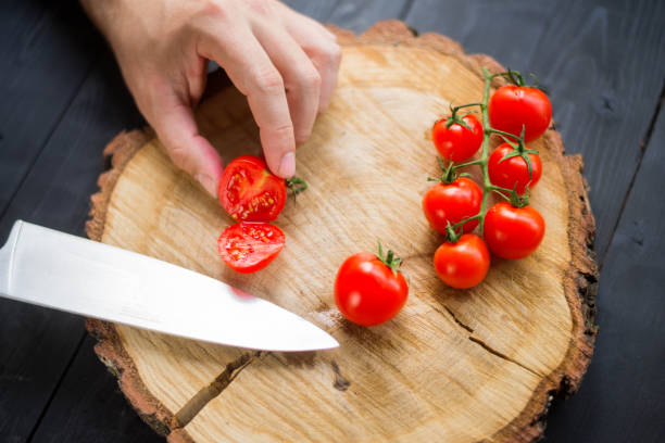 istock Chef slicing cherry tomatoes on a wooden board, close-up. 1175224500