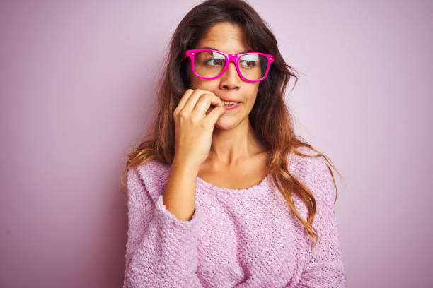 Young beautiful woman wearing fashion glasses standing over pink isolated background looking stressed and nervous with hands on mouth biting nails. Anxiety problem. Young beautiful woman wearing fashion glasses standing over pink isolated background looking stressed and nervous with hands on mouth biting nails. Anxiety problem. nail biting stock pictures, royalty-free photos & images