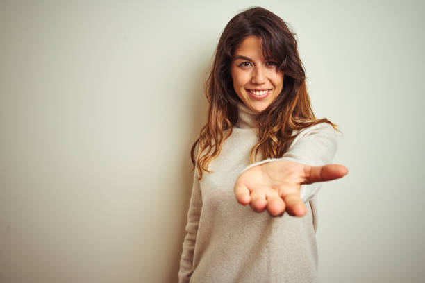 白い孤立した背景の上に立つ冬のセーターを着た若い美しい女性は、手のひらを提供し、援助と受け入れを提供陽気な笑顔。 - give woman ストックフォトと画像