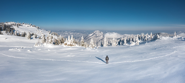 Aerial view on a man hiking through the fresh snow with snowcapped hills in the background.