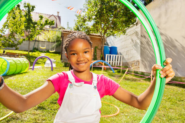 Close portrait of a girl on playground with hoops Beautiful African appearance girl holding color hula hoops and smiling standing on backyard garden playground lawn kids play house stock pictures, royalty-free photos & images