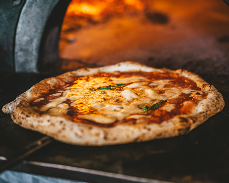 Pizza Margharita Italian Traditional in Stone Wood Oven. Baked with Mozzarella, Tomato Sauce and Basil. Delicious lunch or dinner. Wood on fire in background