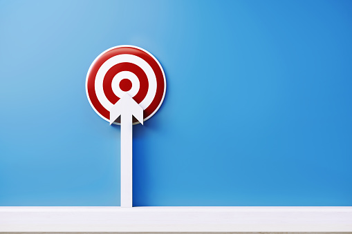 White arrow pointing a red bulls eye target on blue background. Horizontal composition with copy space.