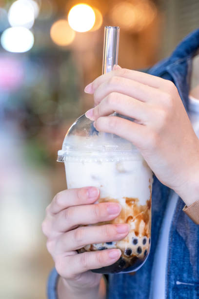 istock Young girl in denim jacket is drinking brown sugar flavored tapioca pearl bubble milk tea with glass straw in night market of Taiwan. 1175236496