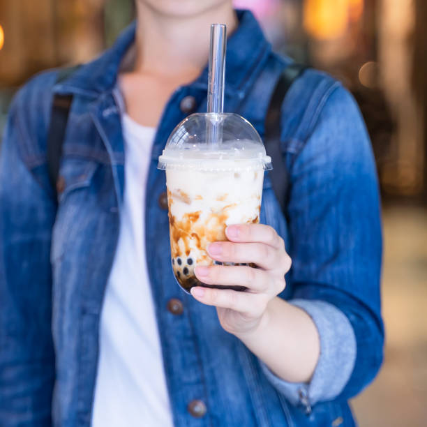 istock Young girl in denim jacket is drinking brown sugar flavored tapioca pearl bubble milk tea with glass straw in night market of Taiwan. 1175236498